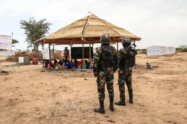 Soldiers look on as a group of children take part in a reading lesson given by an NGO during a field visit by Filippo Grandi, the United Nations High Commissioner for Refugees (UNHCR), in Maroua on April 28, 2022.