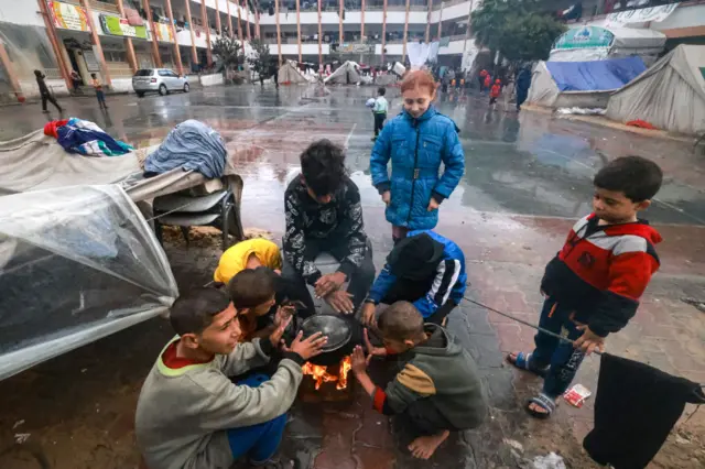 Palestinian children warm up around a fire outside their makeshift tent at a camp set up on a schoolyard in Rafah in the southern Gaza Strip