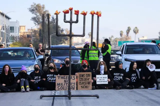 Protesters demanding a ceasefire and an end to US support for Israel's attack on Gaza block morning traffic with a Hanukkiyah, a candlestick with nine branches that is lit to mark Hanukkah