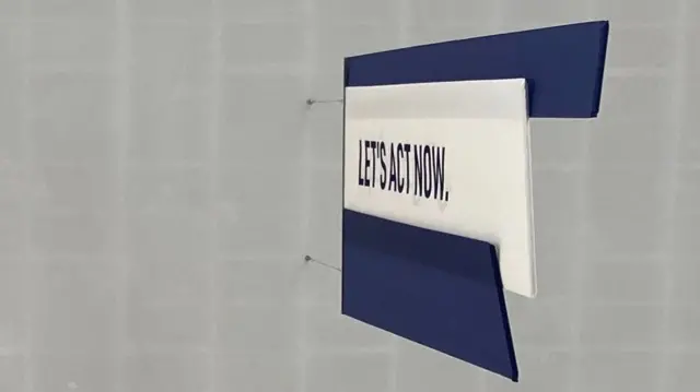 A sign hangs from the ceiling that says "let's act now"