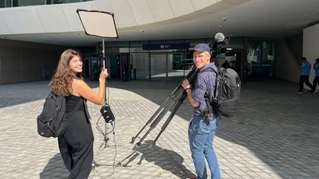 Two journalists run with camera equipment across the complex