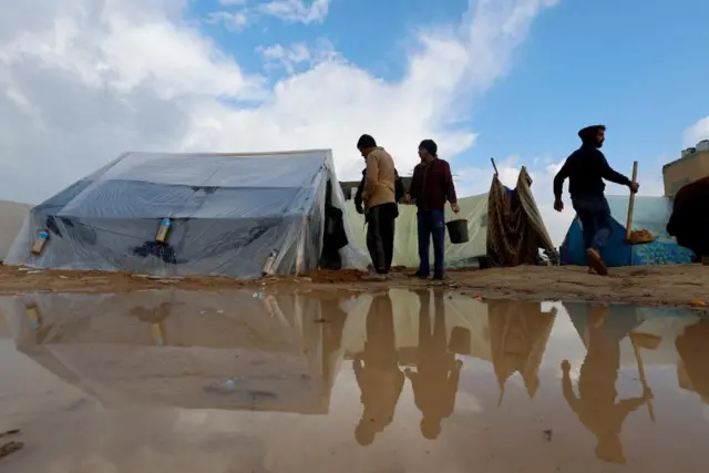 Displaced Palestinians walk next to tents following heavy rains at tent camps