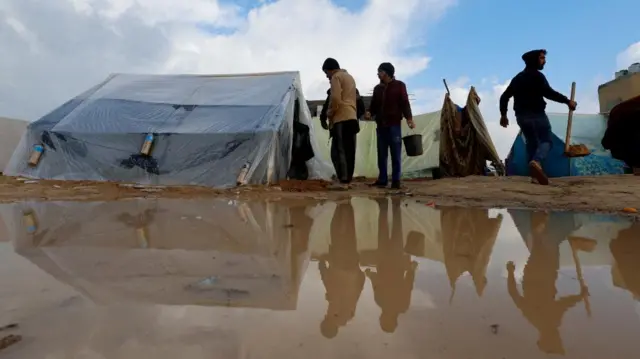 Displaced Palestinians walk next to tents following heavy rains, in a photo taken in Rafah