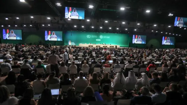 Wide shot of the COP28 room filled with delegates and participants sitting watching the COP team on stage