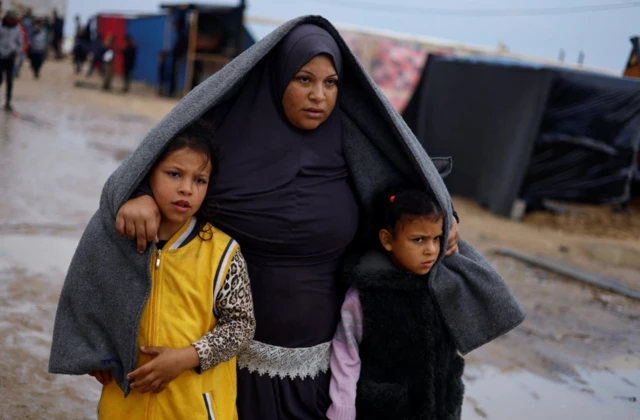 Displaced Palestinian woman takes shelter in Gaza with her children during heavy rainfall