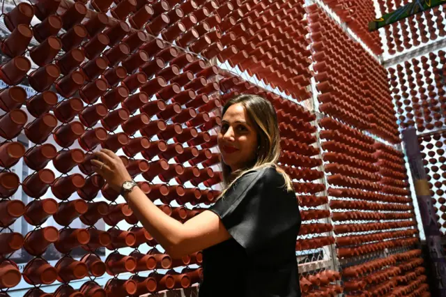 A woman touches a wall of an exhibition stand made with recycled disposable plastic glasses, during the architecture and building fair at the Abidjan exhibition center, on December 13, 2023