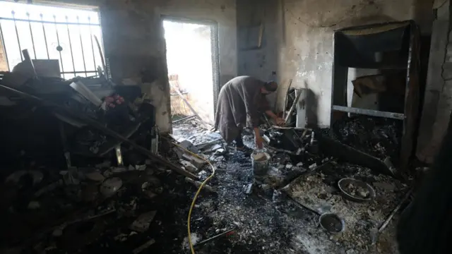 Palestinians inspect damage at a burned house as Israeli forces conduct a raid for a second day at Jenin refugee camp near the West Bank city of Jenin, 13 December 2023