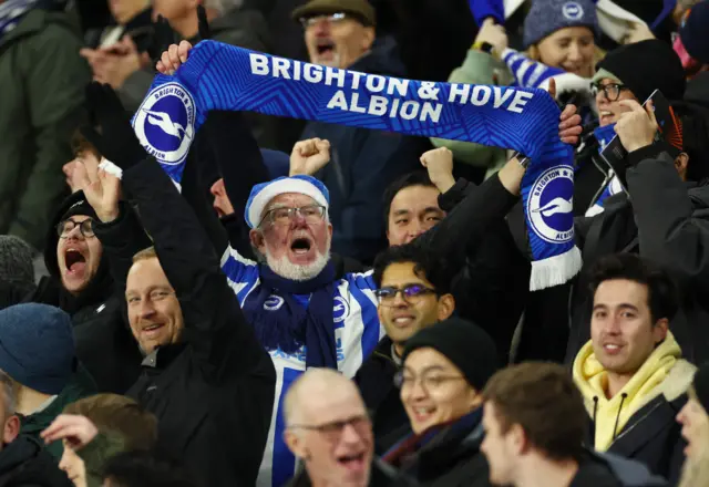 Brighton fan holds their team scarf above their head as fans celebrate around them