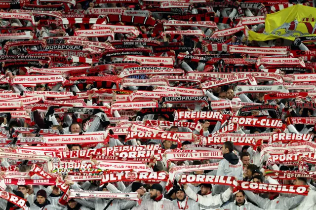 Freiburg fans hold red and white scarves in the stands