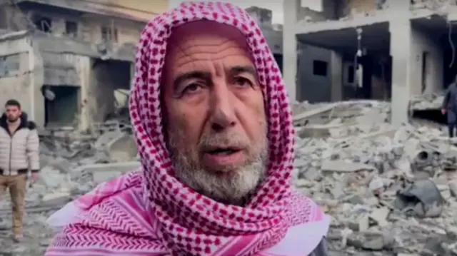 Hassan Al-Byouk stands in front of rubble