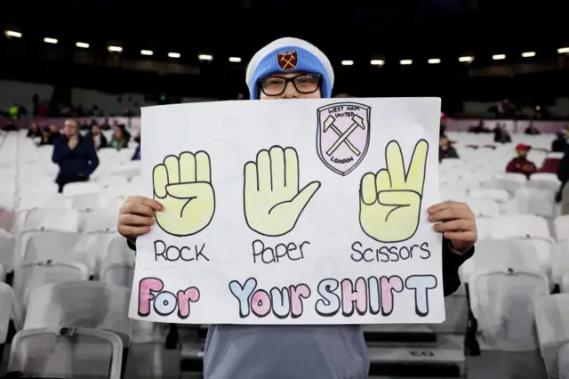 West Ham fan holds a sign which challenges a player to a game of Rock, Paper, Scissors for the chance to win their shirt