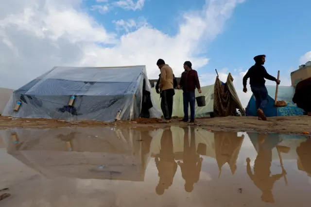 Displaced Palestinians, who fled their houses due to Israeli strikes, walk next to tents following heavy rains at tent camps, as the conflict between Israel and Hamas continues, in Rafah, in the southern Gaza Strip December 13, 2023.