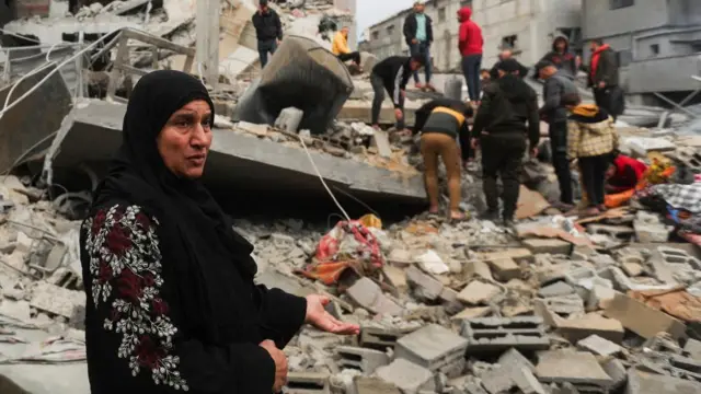 A woman gestures while standing in the ruins of a building