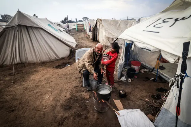 A Palestinian man prepares food for his family outside his tent at a camp for displaced people in Rafah on 13 December