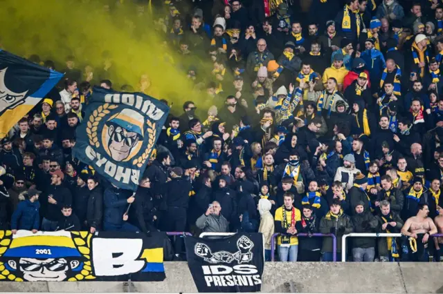 Union Saint-Gilloise fans in the stands with a flags and a yellow flare