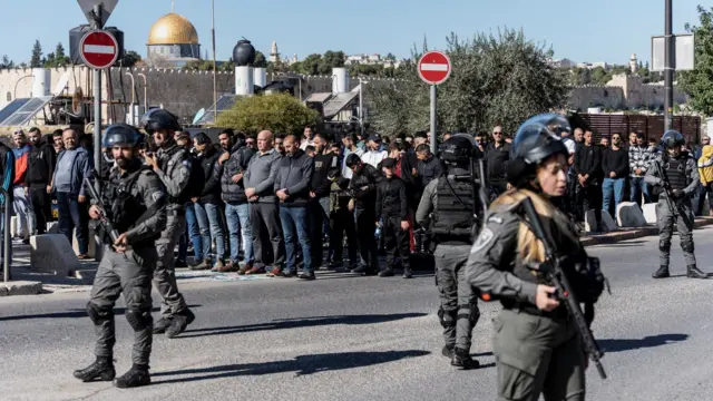 Israeli Border Police officers walk while Muslim Palestinians hold Friday prayers