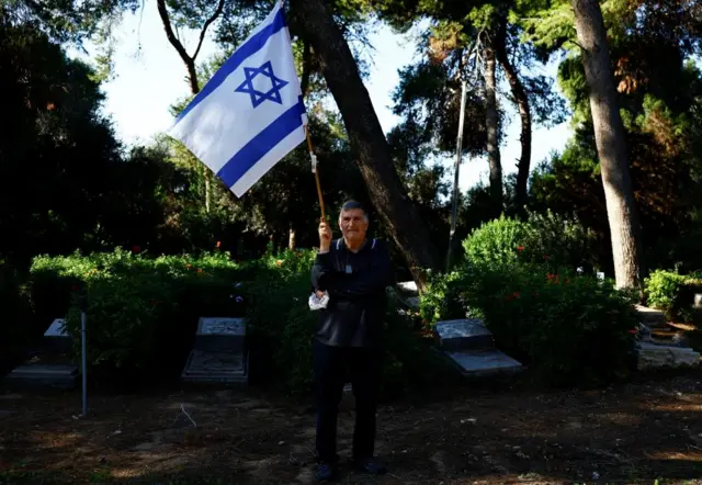 A man holds an Israeli flag as he attends the funeral of Israeli military Sergeant Oz Shmuel Aradi