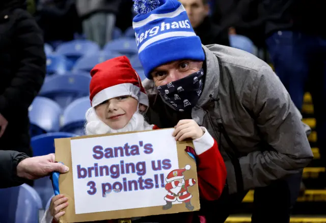 A young fans holds up a sign saying 'Santa please bring us three points'