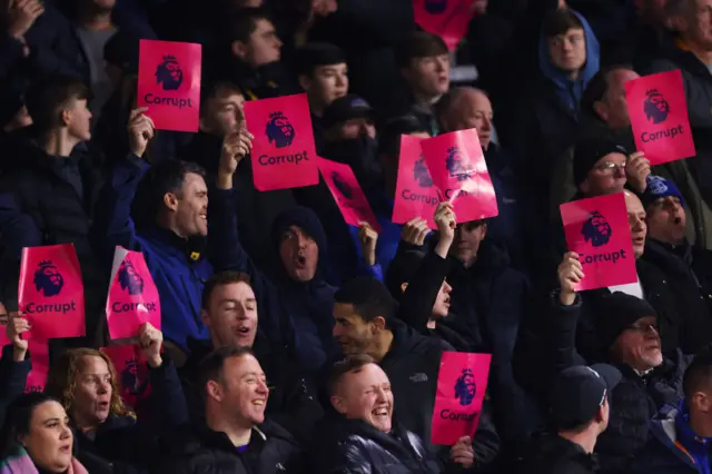 Everton fans hold up signs in protest of the Premier League - the PL logo with the word corrupt underneath.