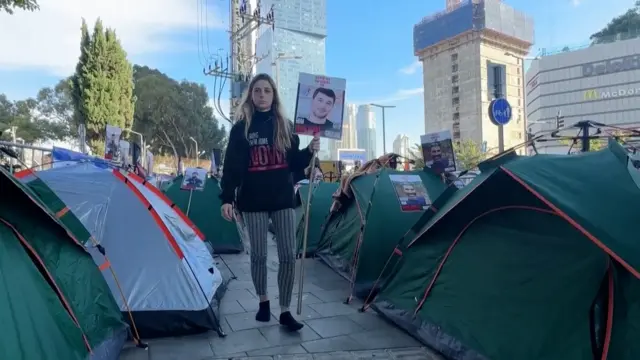 A woman walking with a hostage sign past tents