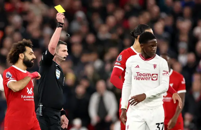 Kobbie Mainoo of Manchester United is shown a yellow card by referee Michael Oliver