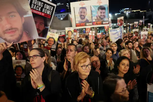 People clapping with signs of hostages being held up