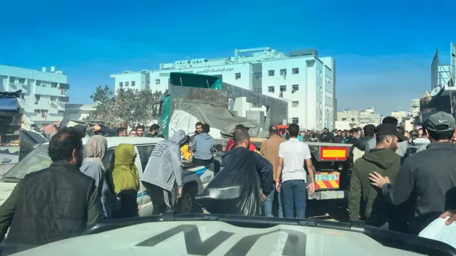 People crowd around the exterior of Al-Shifa Hospital