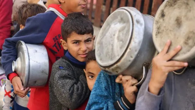 Palestinian children hold pots as they queue to receive food cooked by a charity kitchen, amid shortages in food supplies, as the conflict between Israel and Hamas continues, in Rafah in the southern Gaza Strip December 14, 2023.