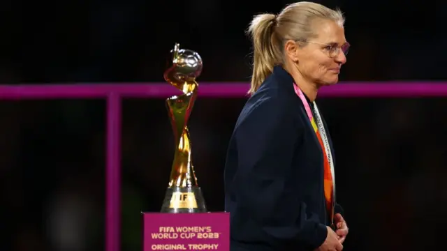 Sarina Wiegman walks past the World Cup trophy