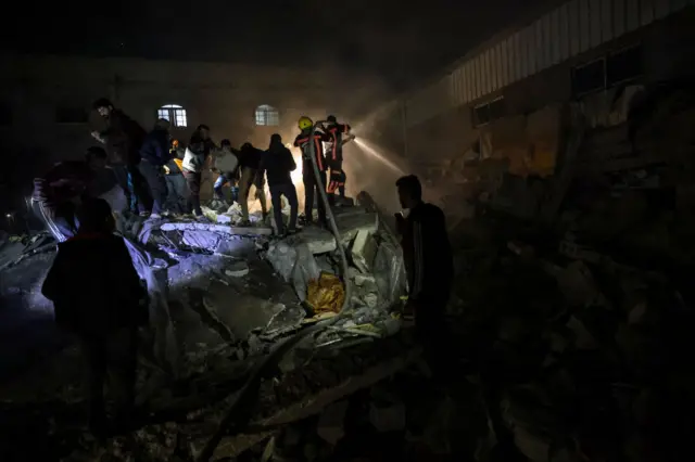 Firefighters and civilians gather at a building by Israeli air strikes on Rafah