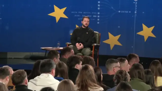 Zelensky sitting in front of a screen with the EU flag