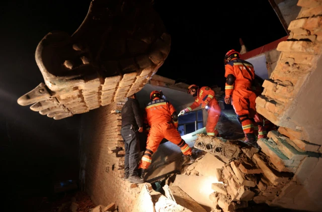 Rescuers in orange outfits climb through damaged buildings in Kangdiao village in Jishishan county
