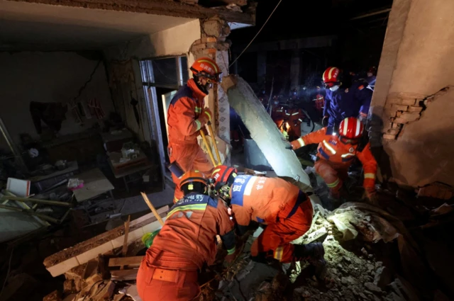 Rescuers in orange outfits climb through damaged buildings in Kangdiao village in Jishishan county