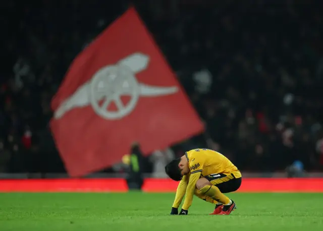 Hwang sinks to the floor as an Arsenal flag waves in the background.