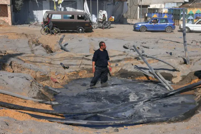 A Palestinian man stands in a crater filled with water after an Israeli airstrike on a main road in southern Gaza