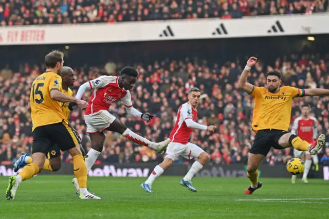 Saka fires at goal as he is closed down by defenders.