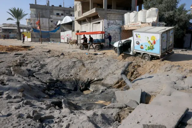 Palestinians drive a cart past a crater on the road damaged during Israel's bombardment of Gaza