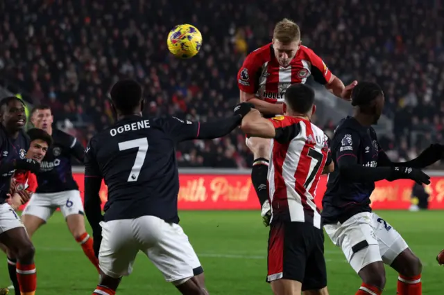 Mee rises highest in the box to head the ball towards goal.