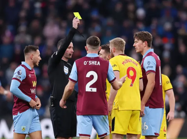 Mcburnie is surrounded by players as he is shown a yellow card.