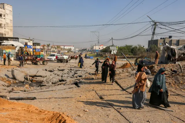 Palestinians walk past a crater following an Israeli airstrike on the main road between Rafah and Khan Younis on the southern Gaza Strip