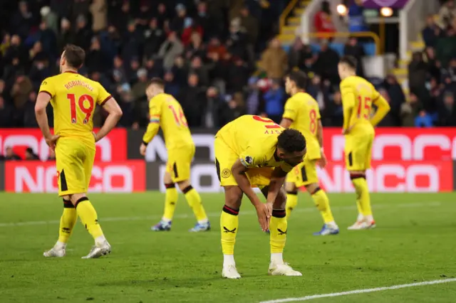 Sheffield United players stand stunned after conceding a fifth goal.