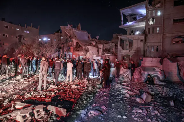 A crowd surrounds a multi-storey building destroyed by an Israeli airstrike on 19/12/23