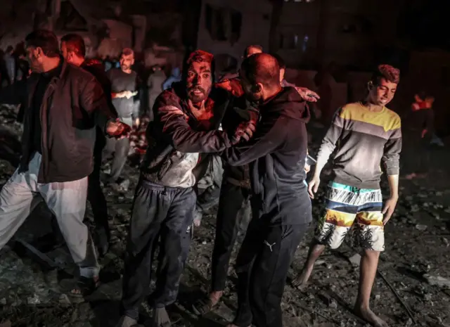 Stunned Palestinians covered in dust and rubble move away from the scene of a building hit by an Israeli strike on 19/12/23