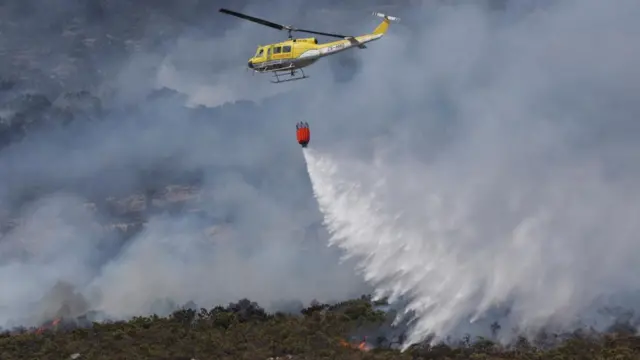 A Huey helicopter from Working on Fire helps extinguish a fire over a mountain at Simon's Town in Cape Town, South Africa, December 20, 2023.