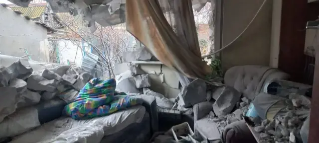 A destroyed apartment in Nikopol where a wall and ceiling had collapsed onto on sofa covered with debris.