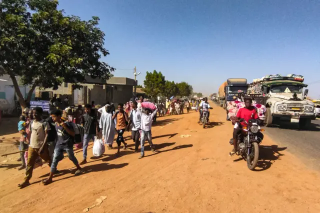 People displaced by the conflict in Sudan walk with their belonging along a road in Wad Madani, the capital of al-Jazirah state, on December 16, 2023.