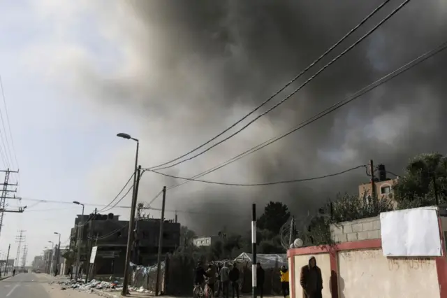 A man walking along a street, smoke rises behind him