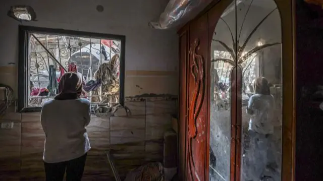 Woman looks out of a window surrounded by debris