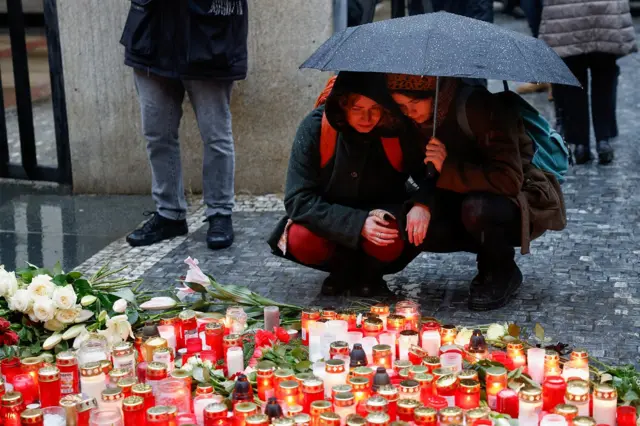 Two women console one another under an umbrella as they look at candles at a vigil for the attacks