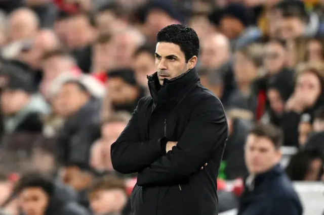 Mikel Arteta stands in front of the dugout with his arms crossed.